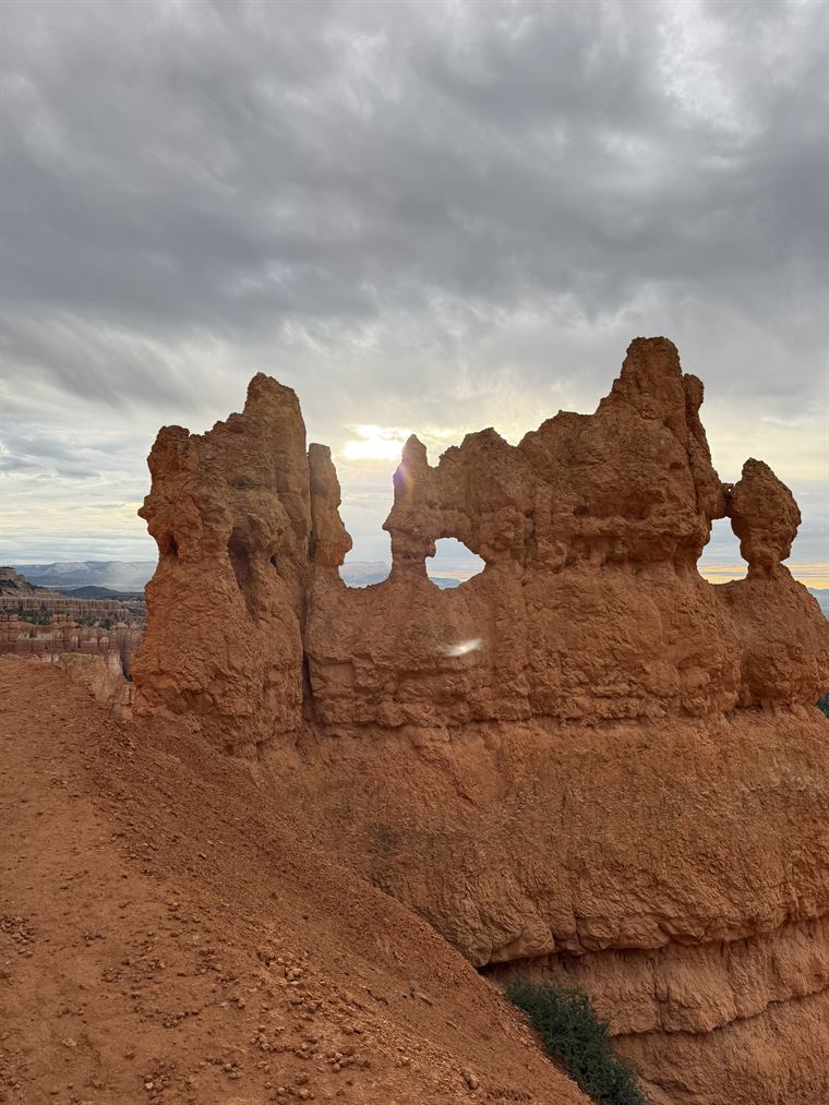 A weathered wall of hoodoos with a window eroded through it, standing against heavy grey cloud.