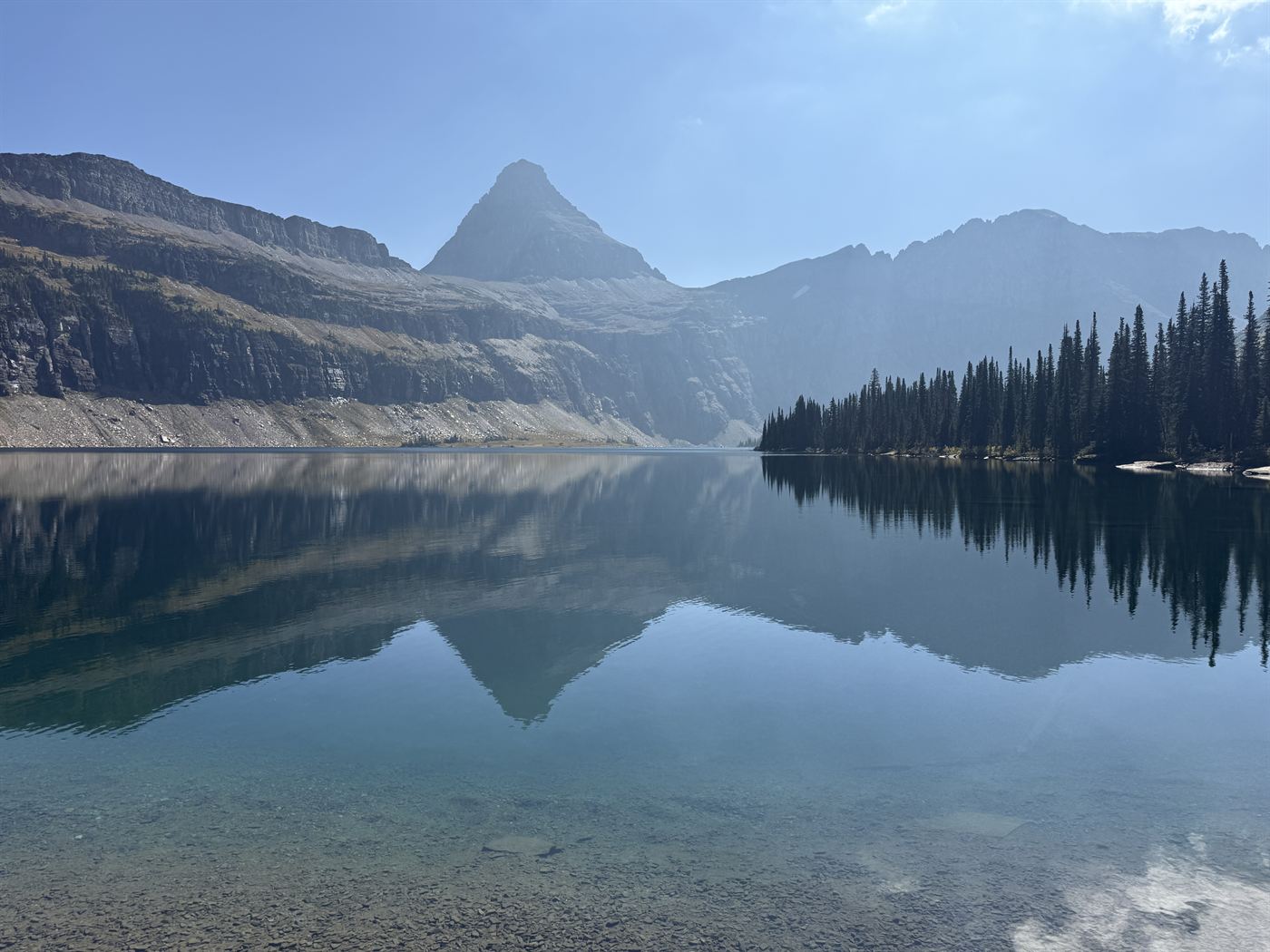 A sharp pyramid-shaped peak and its ridgeline mirrored in the still surface of an alpine lake in Glacier National Park.